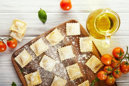 Tasty raw ravioli with flour, cherry tomatoes, sunflower oil and basil on a light wooden background. The process of making Italian ravioli. Copy space. Flat layの写真素材