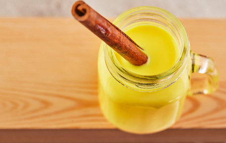 Golden latte turmeric healthy drink in a glass cup. Golden milk with turmeric, cinnamon sticks, turmeric and anise on a wooden background. Turmeric detox tea and ingredients. Copy space. Flat layの写真素材