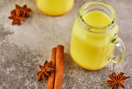 Golden latte turmeric healthy drink in a glass cup. Golden milk with turmeric, cinnamon sticks, turmeric and anise on a gray cement background. Turmeric detox tea and ingredients. copy space.の写真素材