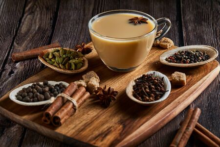 Traditional Indian drink - masala tea with spices. Cinnamon, cardamom, anise, sugar, cloves, pepper on a dark wooden background. Copy space. Side viewの写真素材