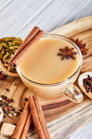 Traditional Indian drink - masala tea with spices. Cinnamon, cardamom, anise, sugar, cloves, pepper on a light wooden background. Copy space. Side viewの写真素材