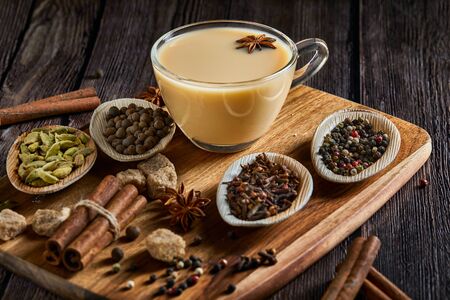 Traditional Indian drink - masala tea with spices. Cinnamon, cardamom, anise, sugar, cloves, pepper on a dark wooden background. Copy space. Side viewの写真素材