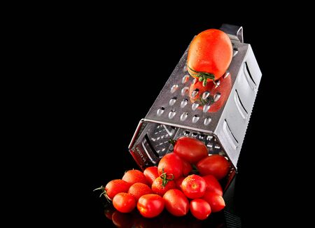 Culinary concept. Large tomato and grater down to small grape cherry tomatoes on a black background. Low calorie food.の写真素材