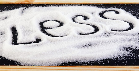 Slice of sugar on a black board and the inscription loess, suggesting a diet and health concept....