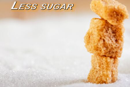 Less sugar text. Cubes of yellow sugar lying on a background of white sugar. Diet and health concepts. Selective focus. Copy space.の写真素材