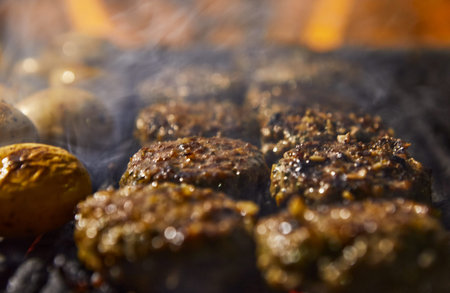 Closeup of kebabs with grilled potatoes in the background and smoke from the barbecue. BBQ party.