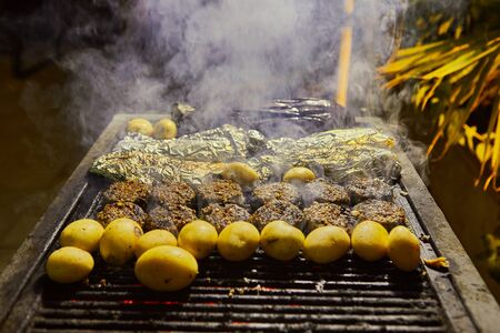Grilled kebabs potato and fish in foil with smoke from the grill. BBQ party.の写真素材