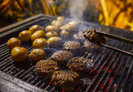 Closeup of kebabs with grilled potatoes in the background and smoke from the barbecue. BBQ party.の写真素材
