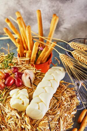 Pigtail-shaped mozzarella with grapes in the hay with bread ears on a blue background. Italian delicacies.の写真素材