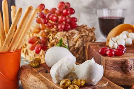 Mozzarella baby brie cheese and mozzarella Fresca with garlic and grapes and a glass of wine on a wooden stand on a gray-blue background. Italian delicacies.の写真素材