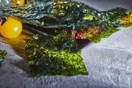 Crispy nori seaweed with cherry tomatoes and dark spices on gray concrete. Japanese food nori. Dried...