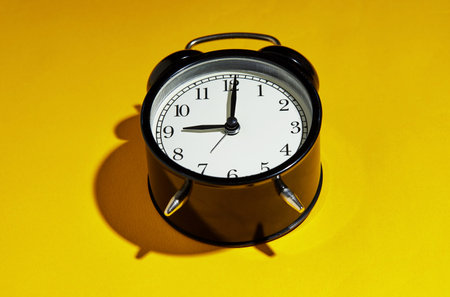 Black alarm clock with a hard shadow on a yellow background.