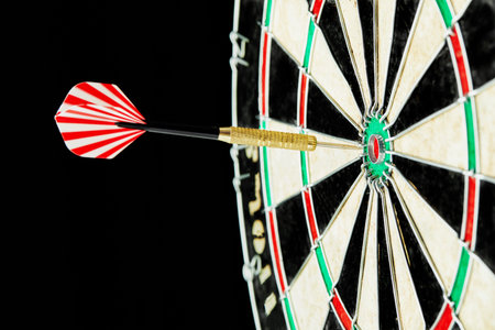 Darts on a black background. 1 dart flies directly to the center of the target. Business center goal...