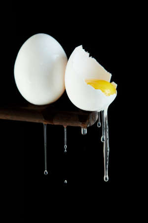 Chicken eggs, one egg is broken in which the yolk is visible and the white flows down on a black background.の写真素材