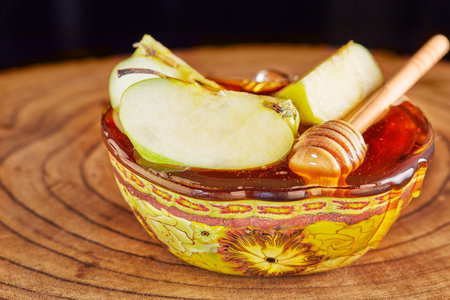 Rosh hashanah - jewish New Year holiday concept. Bowl with honey and sliced apples on a wooden stand.の写真素材