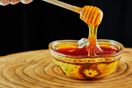 Rosh hashanah - jewish New Year holiday concept. Honey is poured from a stick into an apple-shaped...