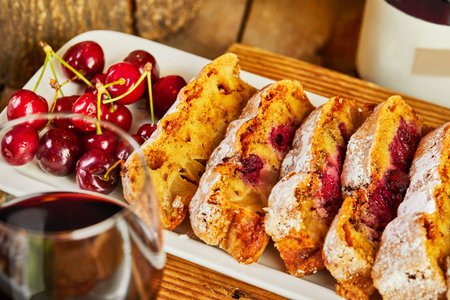 Cherry pie cut into slices on a white plate with cherries and a glass of red wine.の写真素材