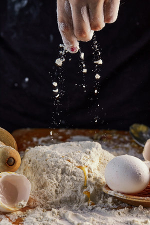 Female hands adding flour to dough, kneading dough for baking. Flour in the air.