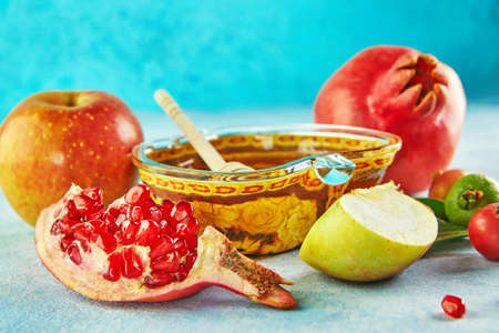 Rosh hashanah - jewish New Year holiday concept. Traditional symbols: Honey jar and fresh apples with pomegranate and shofar -horn on a blue background. Copy space for text.の写真素材
