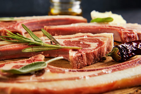 Raw lamb ribs with ingredients for cooking: salt, pepper, olive oil and herbs on a wooden stand....
