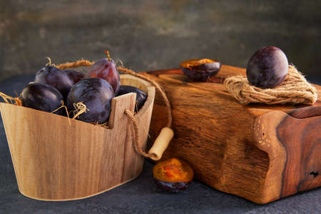 Still life of plums in a wooden basket with hay and a wooden stand on a purple background.の写真素材