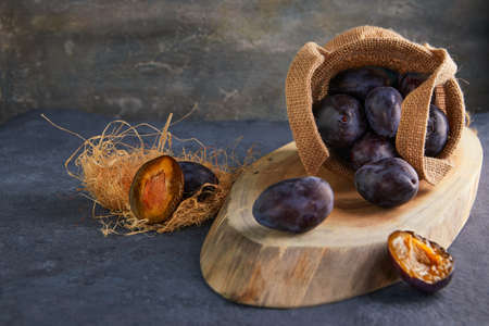 Still life of plums in a bag and hay on a wooden stand on a purple background.の写真素材
