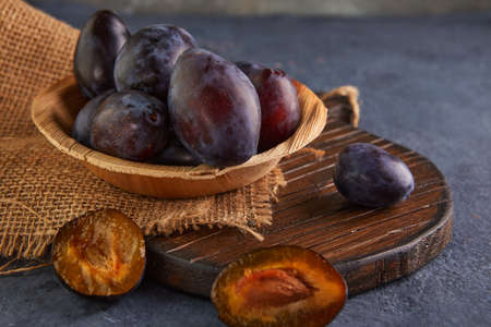 Still life of plums in a wooden plate with burlap on a purple background.の写真素材