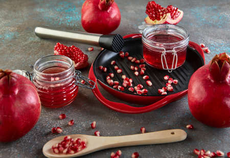 Homemade sweet red pomegranate syrup in jars of pomegranate seeds on a black plate with a red rim.の写真素材