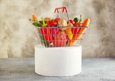 Various vegetables and fruits lying in a supermarket basket on a white podium. Copy space for text.の写真素材