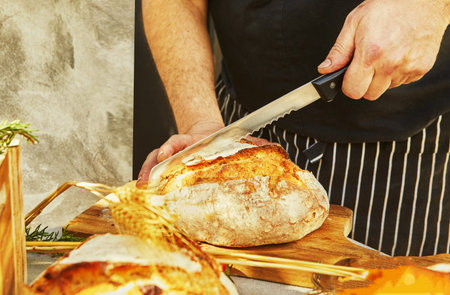 Homemade Italian focaccia bread is cut with a knife on a wooden board.
