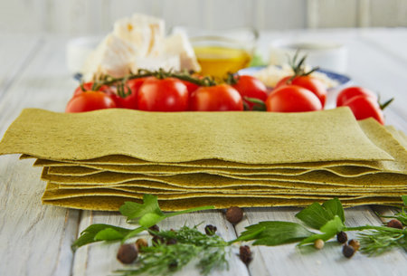 Sheets for cooking lasagna with spinach, stacked in a stack and ingredients: cherry tomatoes,...