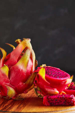 Dragon Fruit - Pitahaya Cut and one whole on a wooden stand against a black wooden background.の写真素材