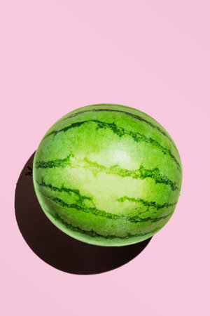 Mini watermelon isolated on a pink background with a hard shadow.