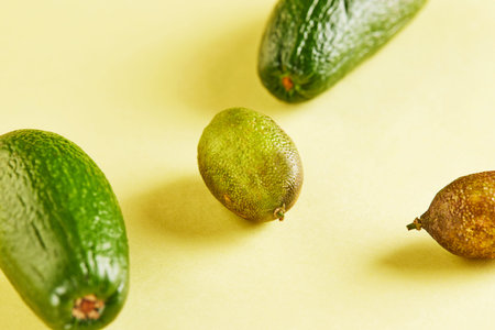 Ripe fresh mini avocados and mini lemons on a yellow background with a shadow.