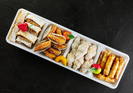 Various types of pastries and cakes with marzipan in white dishes on black concrete.の写真素材