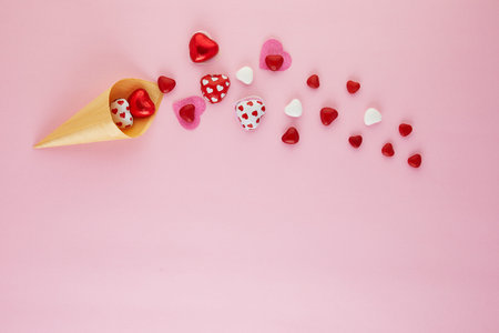 Valentine's Day card with candy hearts flying out of an ice cream cone on a pink background. Top...