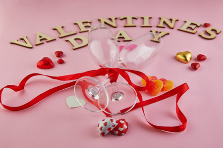 Valentine's day greeting card with glasses of champagne and candy hearts on pink background. Top...