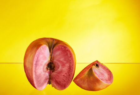 An apple with red flesh inside the cut wedge lies nearby. Yellow background isolated. Exotic fruits, healthy food.の写真素材