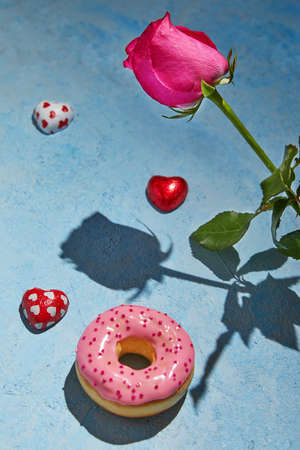 Purple rose with hard shadow and three heart-shaped candies and donut on a blue background. Happy birthday and Valentine's Day greetings.の写真素材