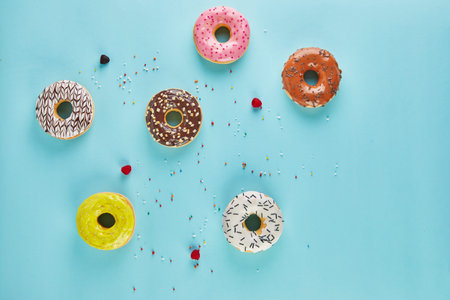 Multicolored donuts with frosting and sprinkles on blue background. Flat lay