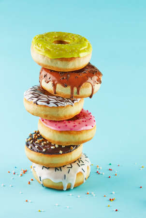 Multicolored donuts with icing and sprinkling stacked in a stack on a blue background.の写真素材