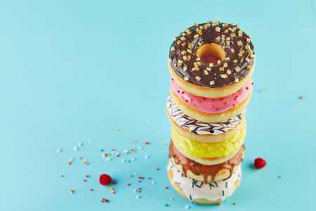 Multicolored donuts with icing and sprinkling stacked in a stack on a blue background.