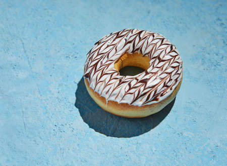 Donut with white frosting and sprinkles on blue background.の写真素材