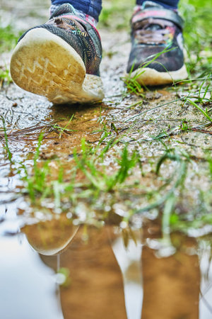 Children's feet in sneakers in the spring forest with reflection in a puddle.