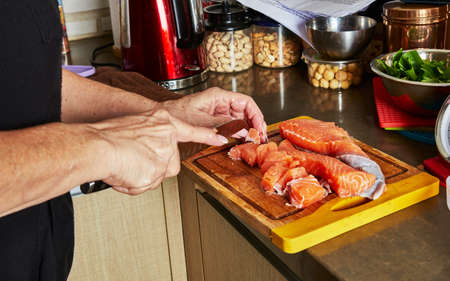 Cooking at home in the kitchen according to recipe from the Internet. Woman cuts fresh salmon with knife on cutting board. Step by step recipe.の写真素材