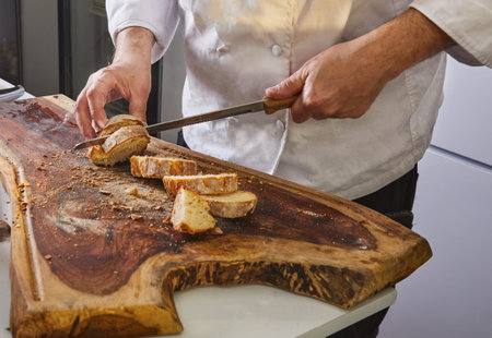Homemade Italian focaccia bread is cut with knife on wooden board.