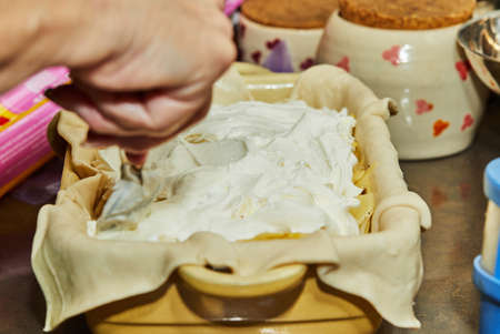 Cooking at home in the kitchen according to recipe from the Internet. Woman adds sour cream to potato pie with onions. Step by step recipe.の写真素材