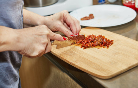 Woman slices sun-dried tomatoes on wooden board to make sun-dried tomato muffinsの写真素材