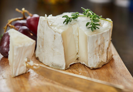 Selected French cheeses with grapes, on wooden board with rosemary and knife