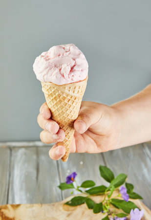 Hand holding waffle cone with ice cream on gray background with flowers